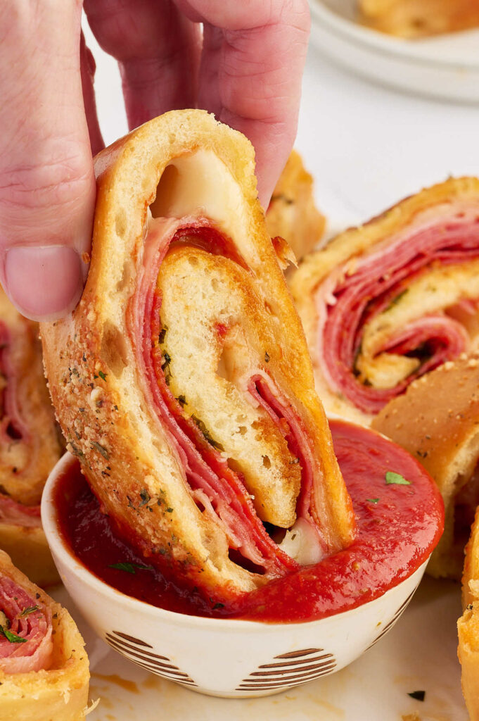 Close-up of a meat stromboli slice dipped in marinara sauce.