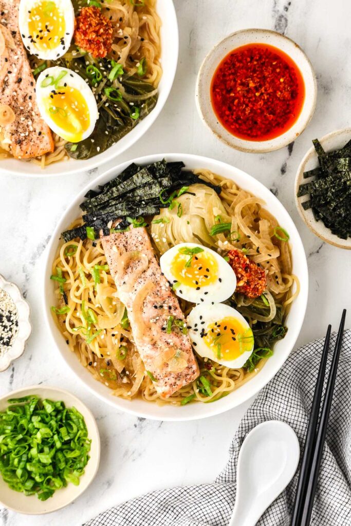 Overhead bowl of salmon ramen with bok choy, noodles, soft-boiled eggs, nori, and chili crisp.
