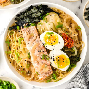 Close-up of a bowl of miso salmon ramen topped with salmon, soft-boiled eggs, bok choy, nori, green onions, and chili crisp.