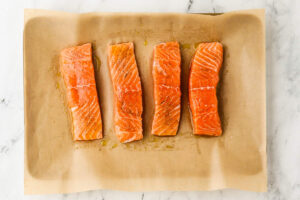 Four seasoned salmon fillets arranged on a parchment-lined baking sheet before roasting.