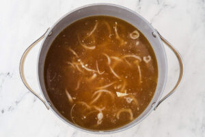 Miso broth with sliced onions in a pot before the bok choy and noodles are added.