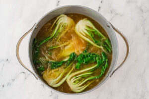 Miso ramen broth with halved baby bok choy simmering in a pot.