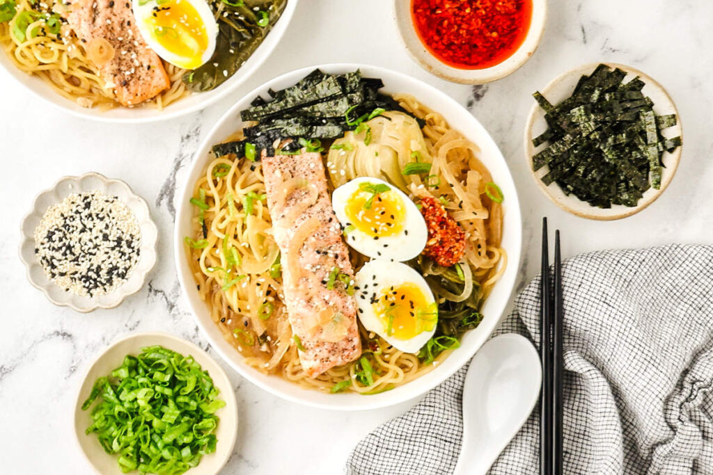 Overhead view of miso salmon ramen with noodles, salmon, bok choy, soft-boiled eggs, nori, green onions, and chili crisp.