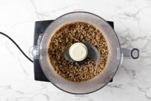 Food processor with finely ground nuts, viewed from above on marble.