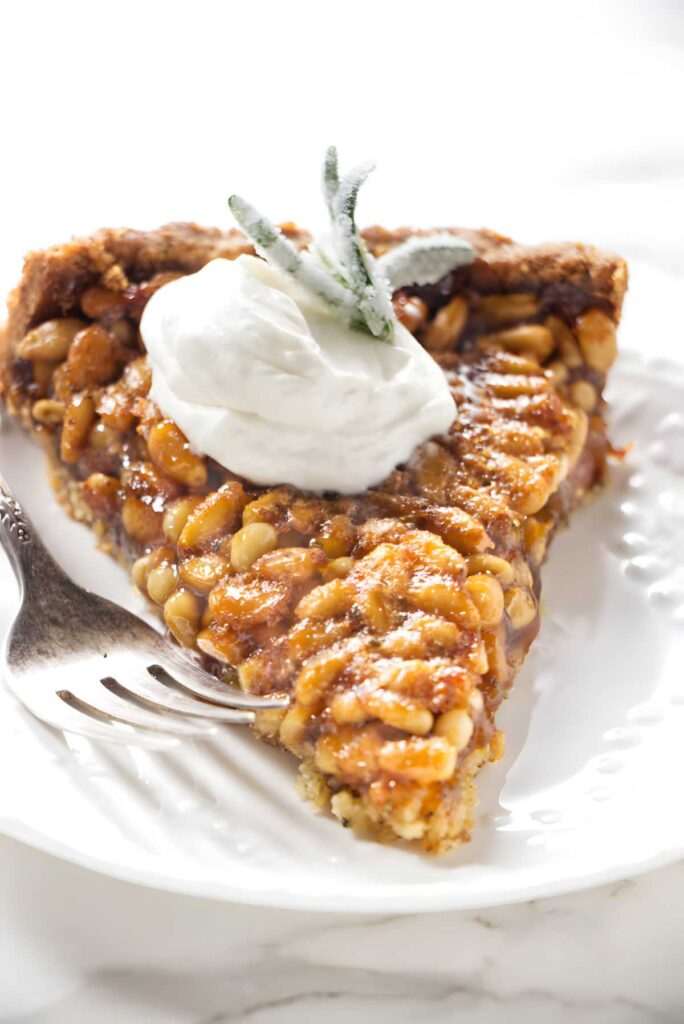 Pecan pie slice with whipped cream and mint on a white plate.