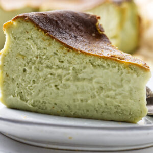Pistachio cheesecake slice served with a spoon and the remaining cake in the background.