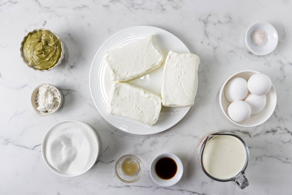 Ingredients for pistachio Basque cheesecake arranged on a marble countertop.