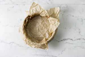 An 8-inch springform pan lined with crumpled parchment paper for pistachio cheesecake.