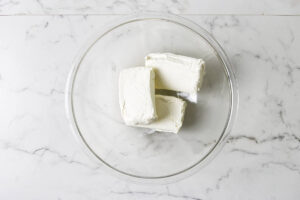 Cream cheese in a glass mixing bowl for pistachio cheesecake.