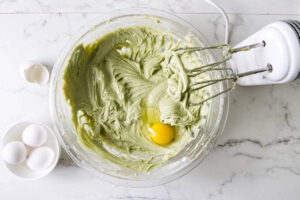 Egg being mixed into green pistachio cheesecake batter.