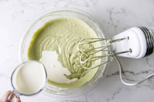 Heavy cream being poured into pistachio Basque cheesecake batter.