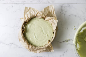 Smooth pistachio cheesecake batter spread in a parchment-lined springform pan.