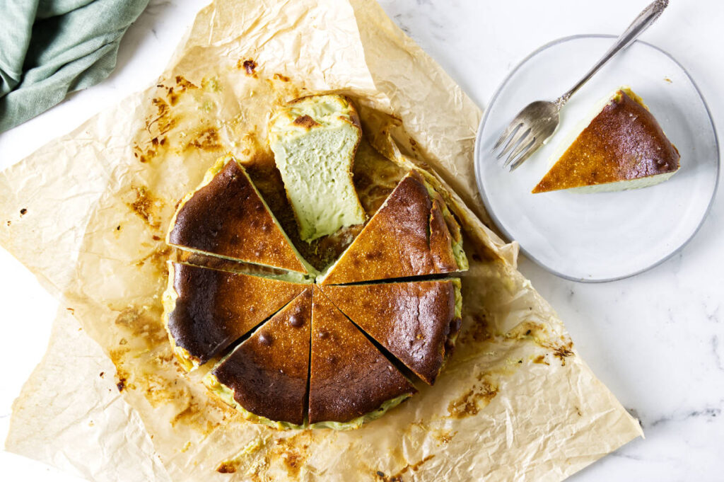 Pistachio Basque cheesecake cut into wedges with a slice served on a plate.