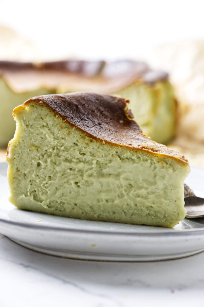 A thick slice of San Sabastian pistachio cheesecake with a deeply browned top on a white plate.