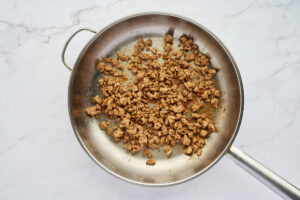 Browned Italian sausage crumbles in a skillet for sausage ricotta calzones.