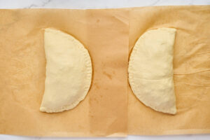 Two sealed calzones filled with sausage, spinach, and ricotta on parchment paper.