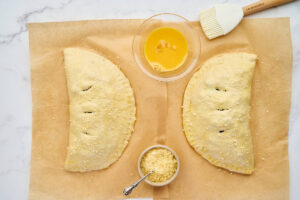 Unbaked calzones brushed with egg wash and sprinkled with Parmesan cheese.