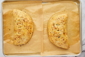 Baked sausage ricotta calzones on a parchment-lined baking sheet.