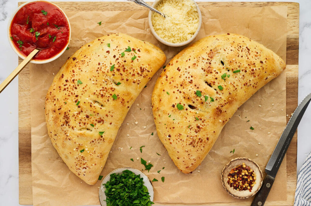 Two golden sausage ricotta calzones served with marinara sauce, Parmesan, and parsley.