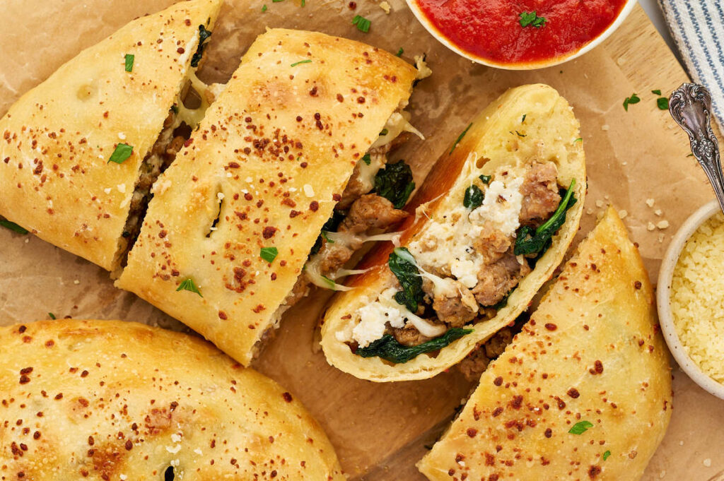 Baked sausage ricotta calzones cut into pieces and served with marinara sauce.