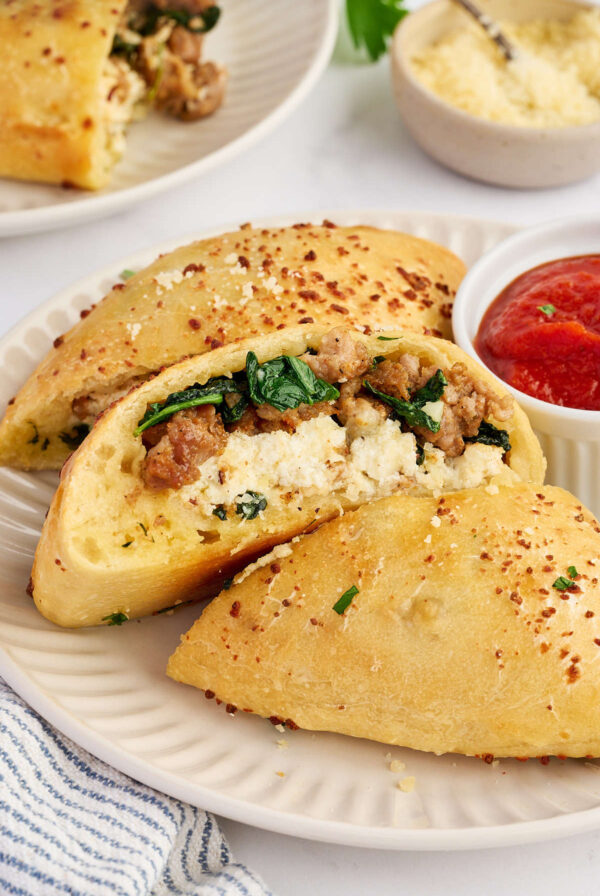 Sliced sausage and ricotta calzones served on a plate with marinara sauce.