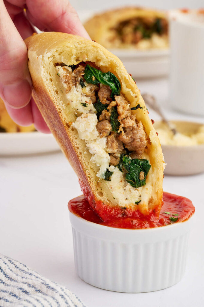 A sausage ricotta calzone held open to show the sausage, spinach, and ricotta filling.
