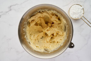 Creamed butter and sugar in a mixing bowl with a measuring cup.