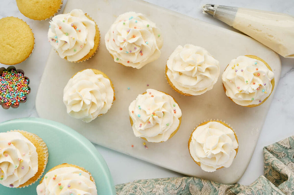 Vanilla cupcakes with white frosting and colorful sprinkles.