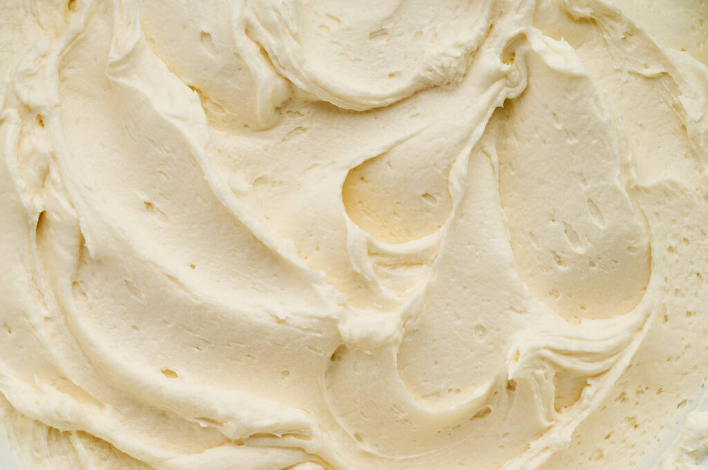 Close-up of smooth, cream-colored frosting with decorative swirls.