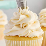 Metal piping tip swirls white frosting onto a yellow cupcake.
