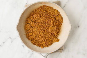 Crumbled cooked food in a wide frying pan on marble.