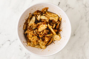 White bowl of cinnamon-tossed sliced apples and raisins.