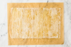 Buttered layers of thin phyllo dough on parchment paper.