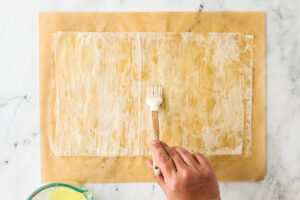 Hand using a pastry brush to butter a sheet of phyllo.