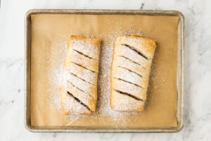 Two powdered sugar-dusted fruit strudels sliced on a baking sheet.