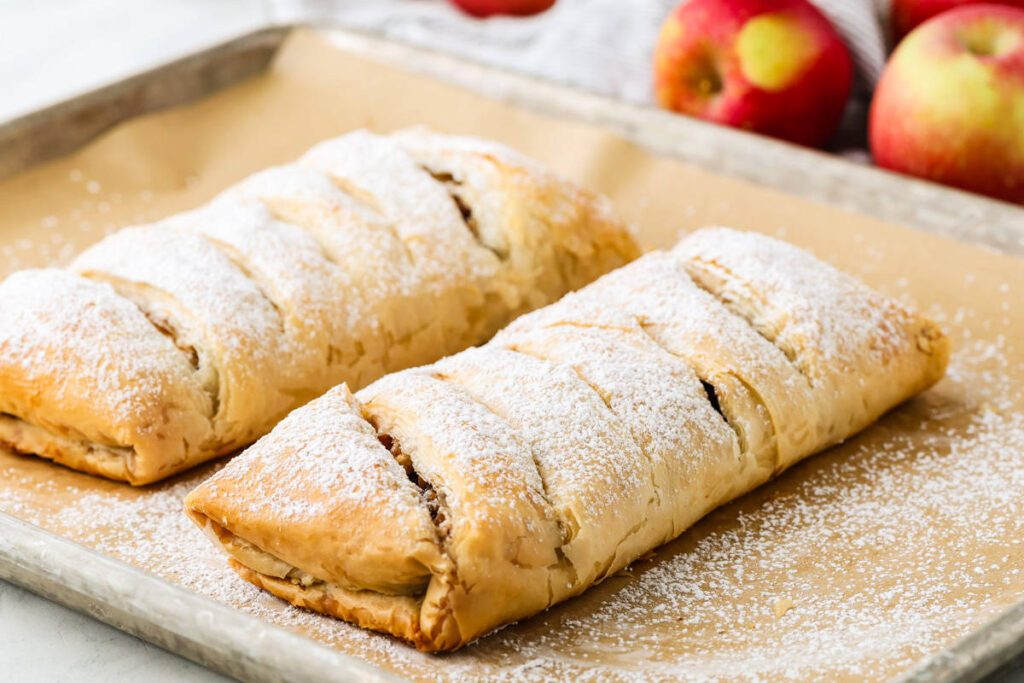 Two powdered sugar-dusted apple strudels on a baking sheet.