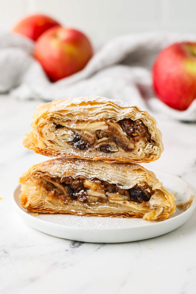 Two slices of apple strudel stacked on a small white plate.
