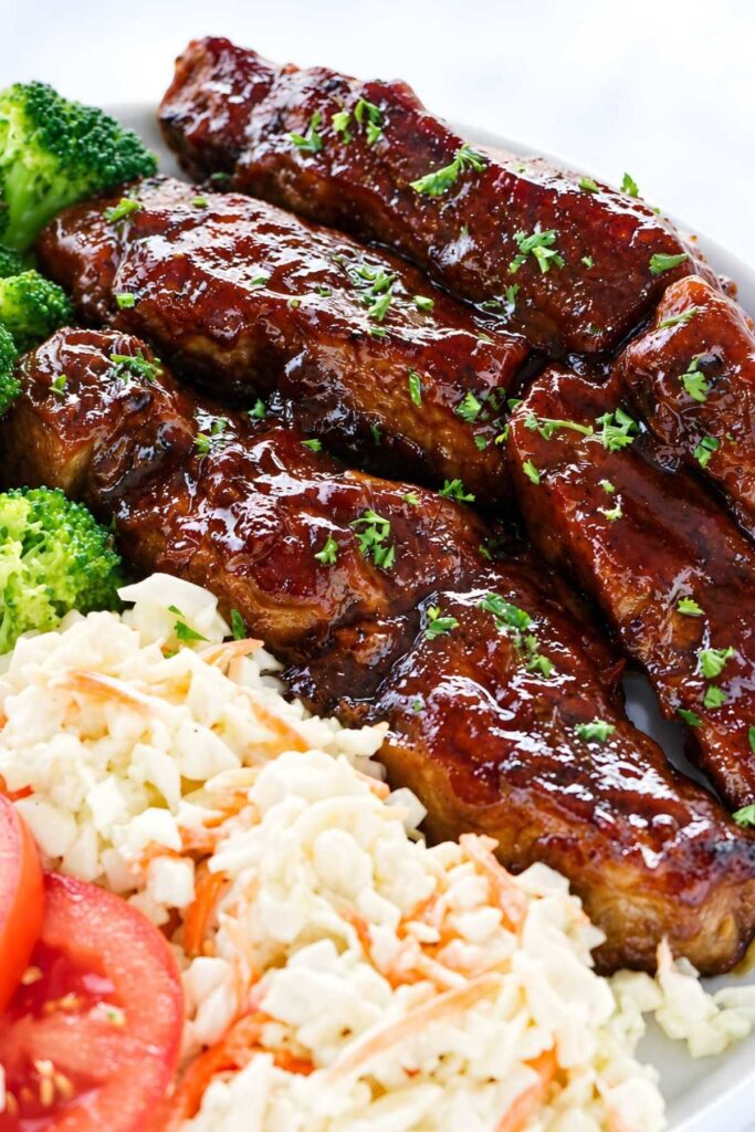 BBQ ribs served with broccoli, coleslaw, and tomato slices on a plate.