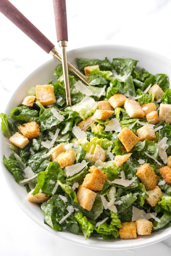 Caesar salad with croutons and shaved cheese in a white bowl.