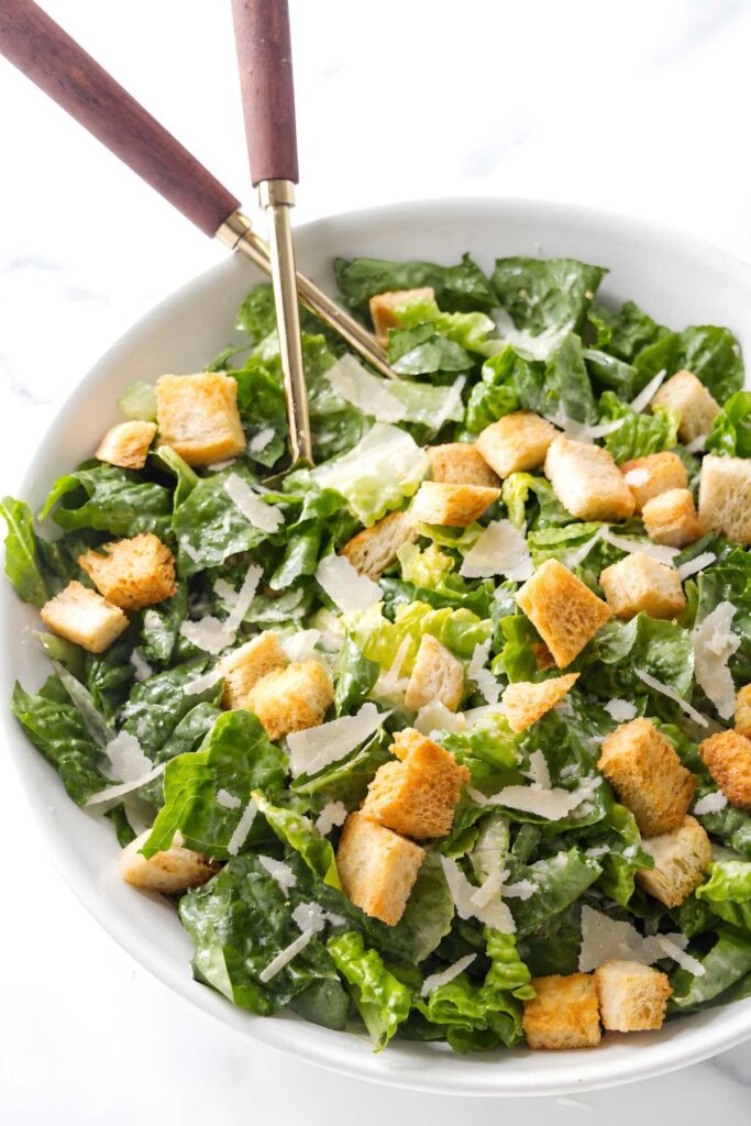 Caesar salad with croutons and shaved cheese in a white bowl.