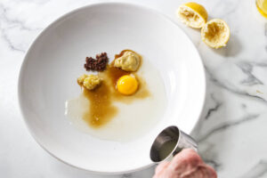 Egg yolk, mustard, minced garlic, and liquids in a white bowl.