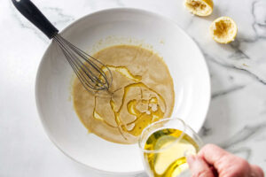 Oil being poured into a white bowl of whisked dressing.