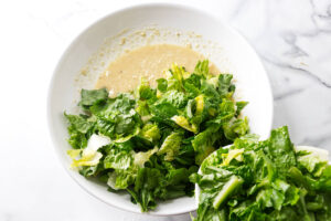 Chopped romaine lettuce being added to a bowl with creamy dressing.