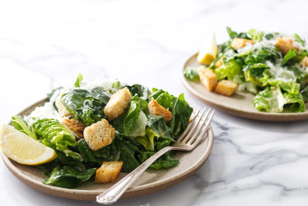 Two plates of Caesar salad with croutons, parmesan, and lemon wedges.