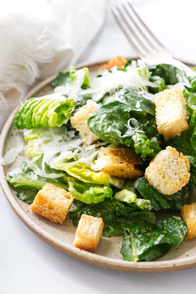 Caesar salad with croutons and shaved cheese on a plate.