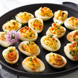 Platter of deviled eggs garnished with paprika and chives.