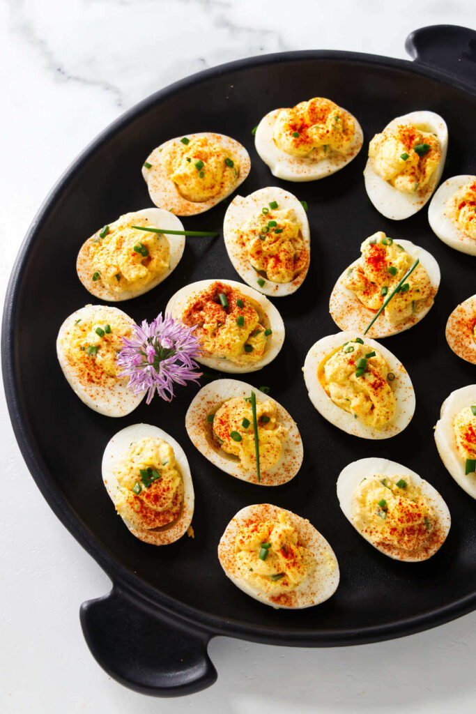 Paprika and chive topped deviled eggs on a black platter.