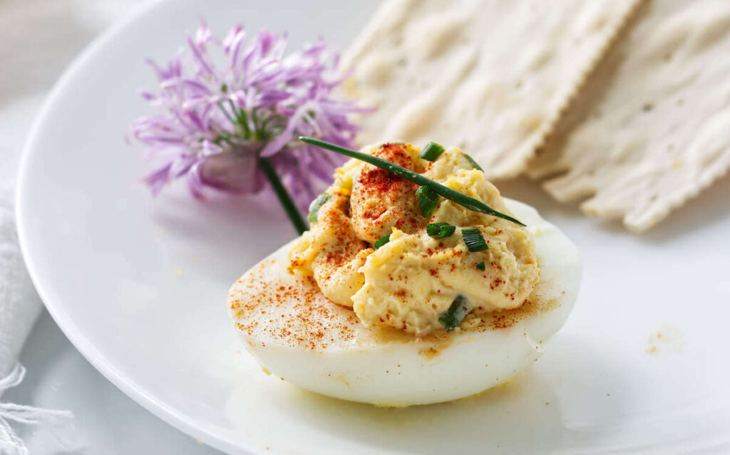 Deviled egg with chives and paprika next to a flat cracker.