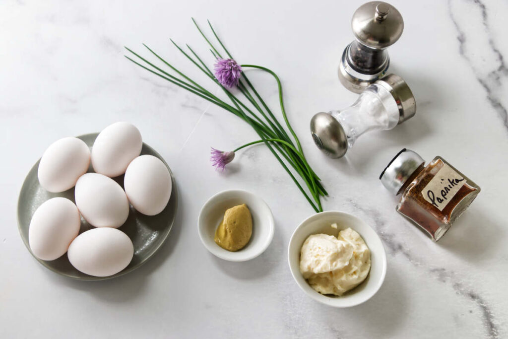 Eggs with chives, mustard, mayonnaise, paprika, salt, and pepper on marble.