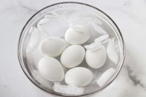 Hard-boiled eggs cooling in a glass bowl of ice water.